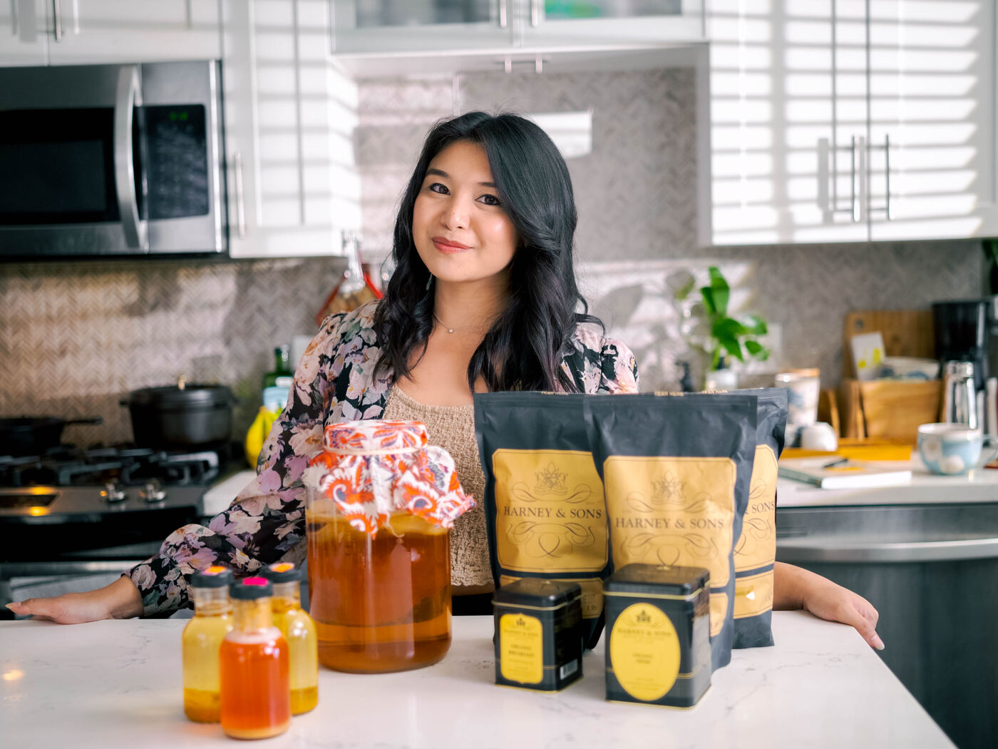 Angelica in her kitchen with a jar of kombucha and the Kombucha Crafter's Logbook